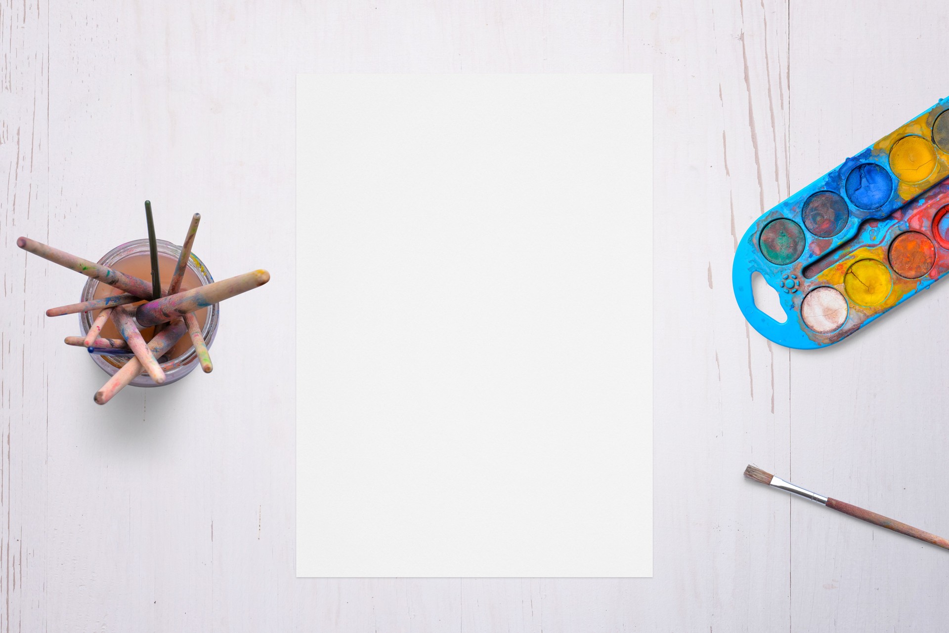 Blank white paper on desk, surrounded by brushes and watercolors. Ideal for artistic creativity, painting concepts, or design themes.