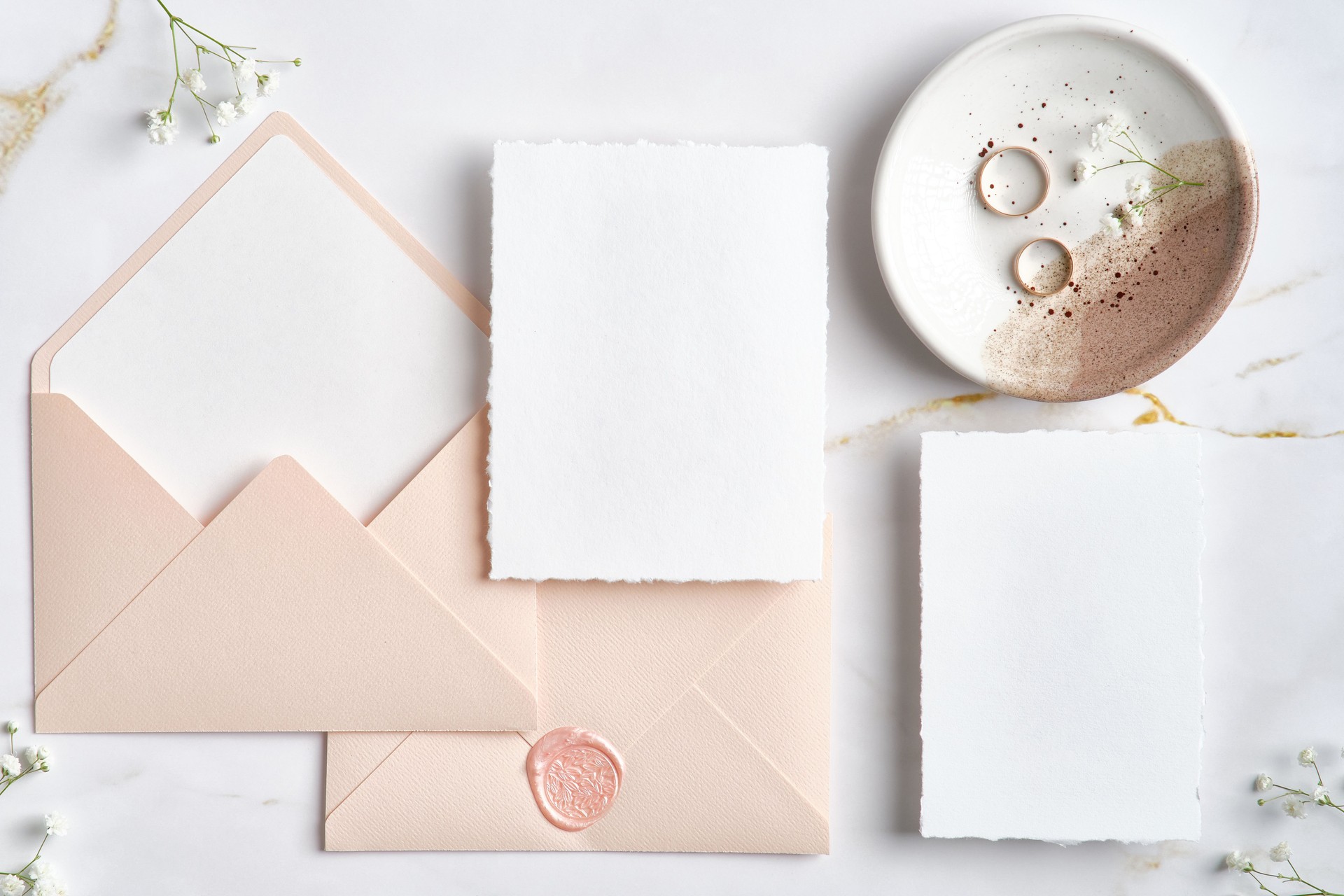 Elegant wedding stationery top view. Flat lay blank paper card, pink envelopes, golden rings on marble desk.